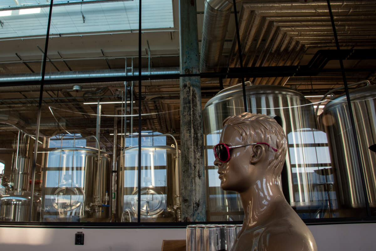 Utsikt över ett bryggeri genom stora fönster med en statyett av en man i förgrunden.